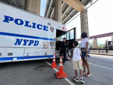 a police truck during the day on Randall's Island with three people standing next to it